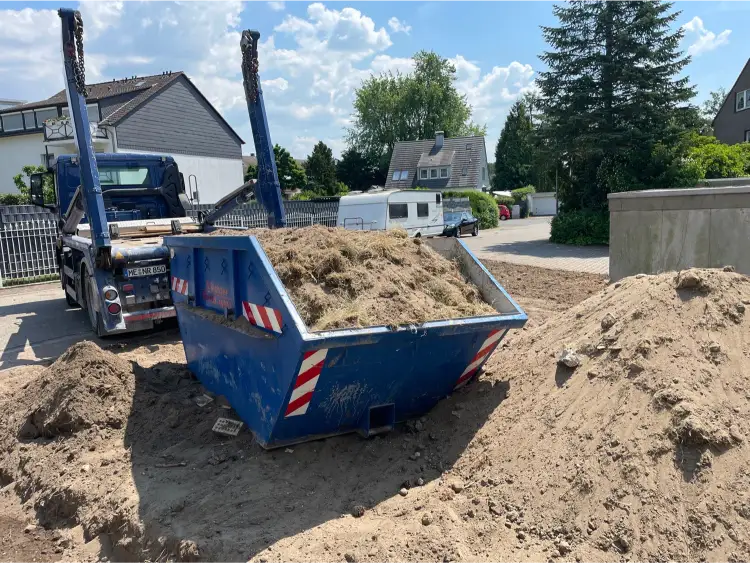 Ein prall gefüllter Container mit Boden, welcher mit Grasnarben und Wurzeln verunreinigt ist.