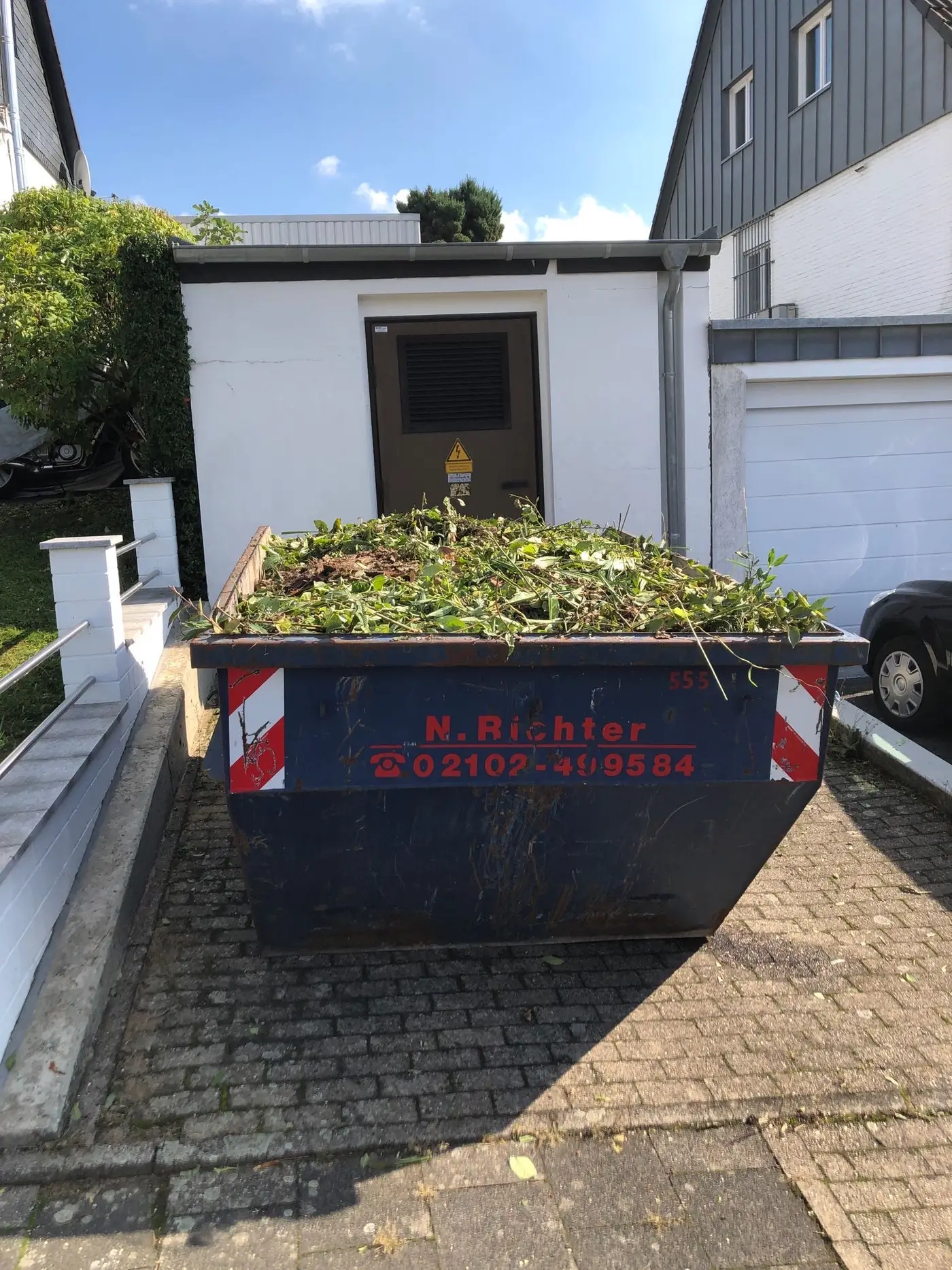 Ein Container von Richter Container in der Einfahrt beim Kunden gefüllt mit Gartenabfällen